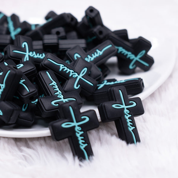 front view of a pile of Black Cross with Teal writing Silicone Focal Bead Accessory