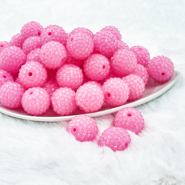 front view of a pile of 20mm Bubblegum Pink beads featuring a rhinestone covered surface pictured on a white dish and white background