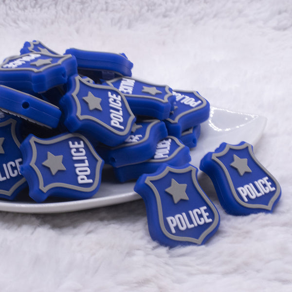 front view of a pile of Blue Police Badge Silicone Focal Bead Accessory - 25mm x 30mm
