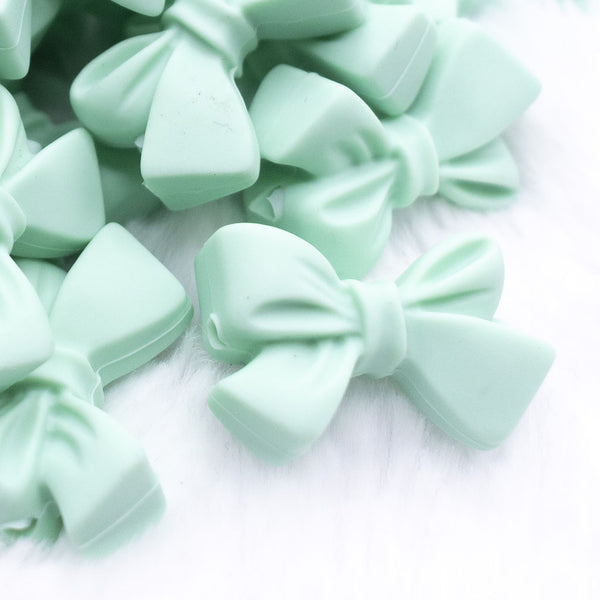 Close up view of a pile of 27mm Spearmint Green Bow Knot silicone bead